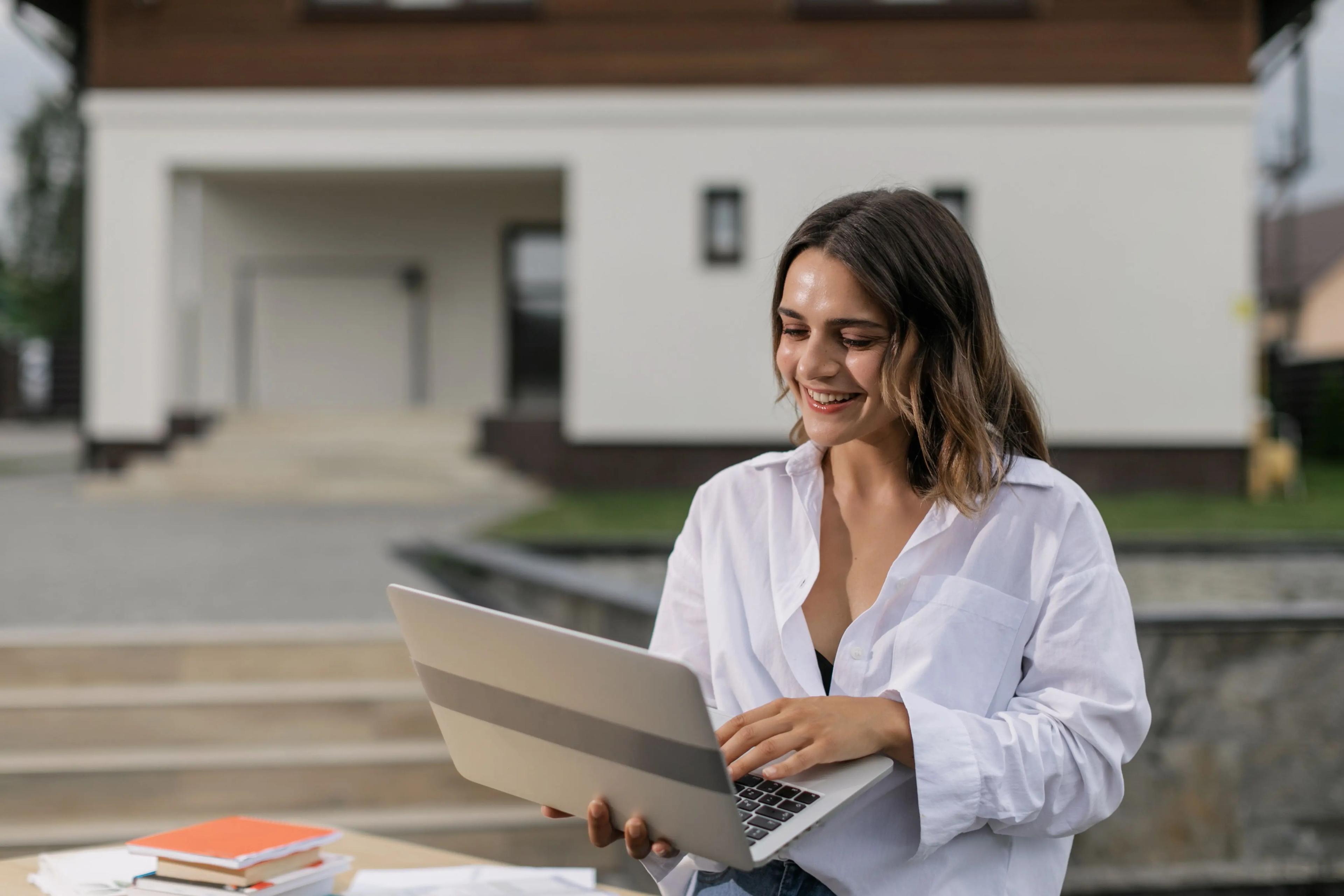 Courtière souriante qui travaille sur son portable devant une maison