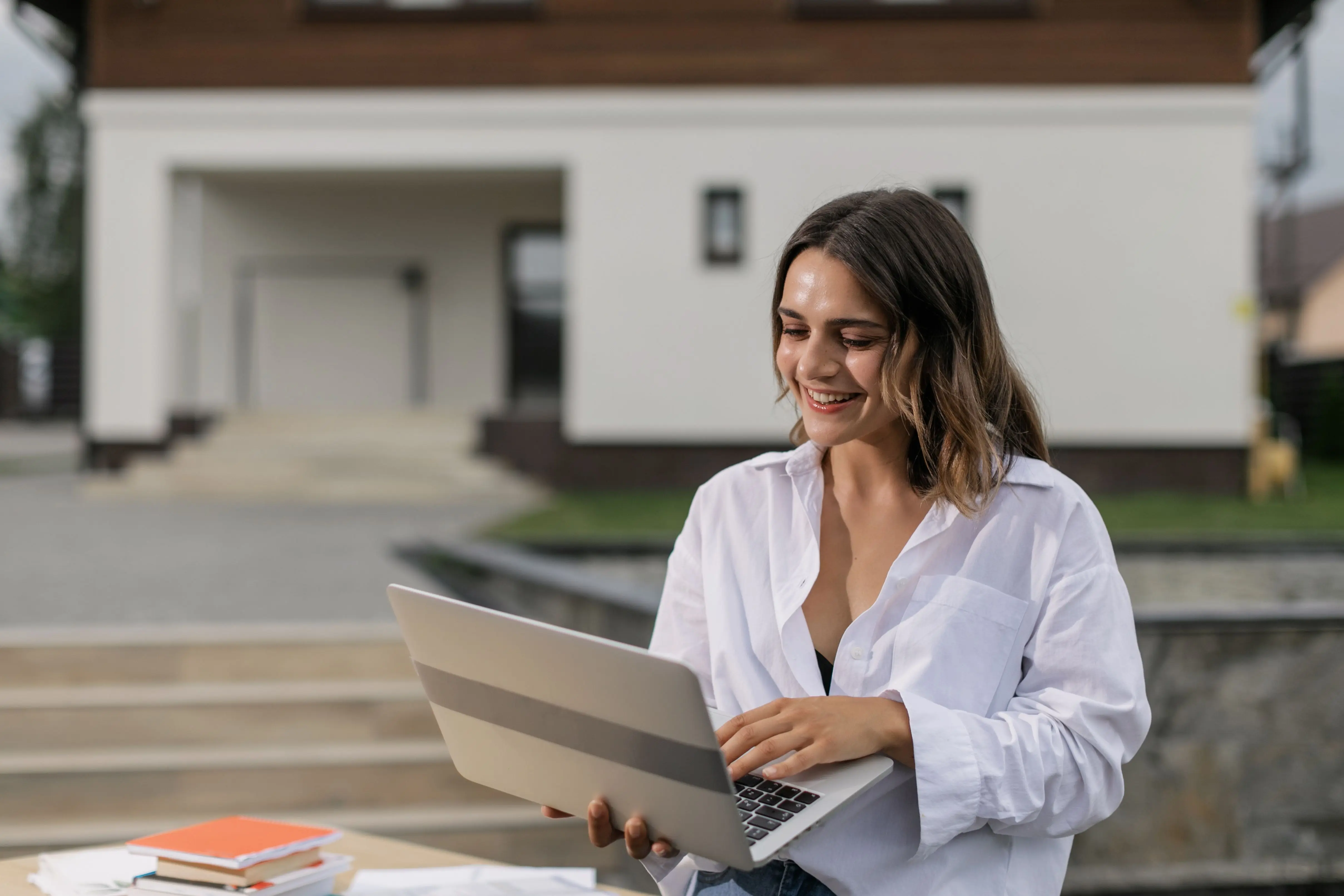 Courtière souriante qui travaille sur son portable devant une maison